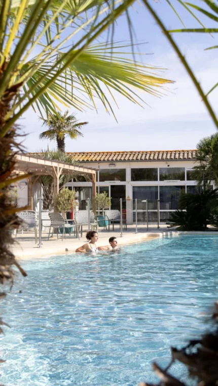 Piscine entourée de palmiers, personnes nageant.